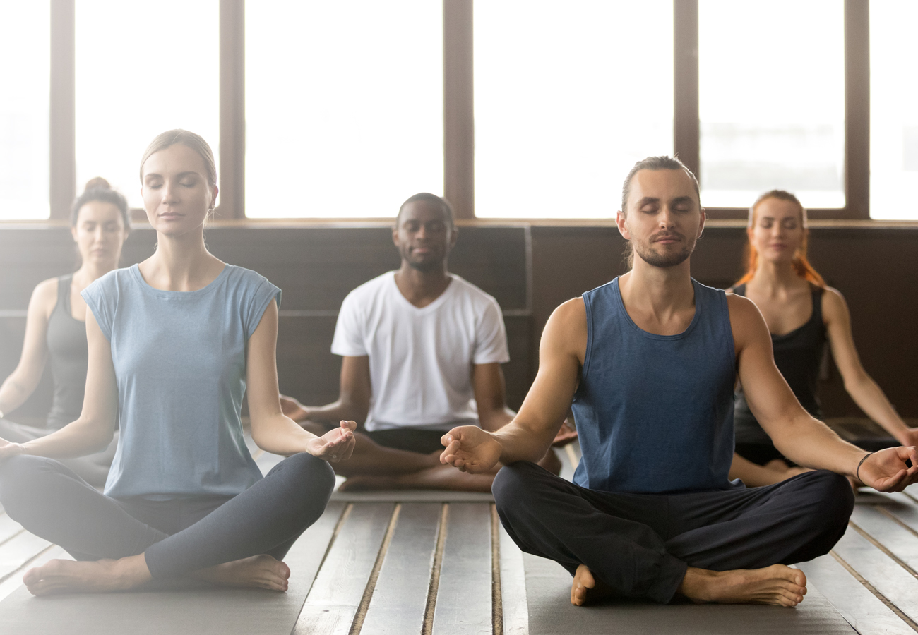 Group of 5 people sat on the floor cross legged doing pilates pose and meditating